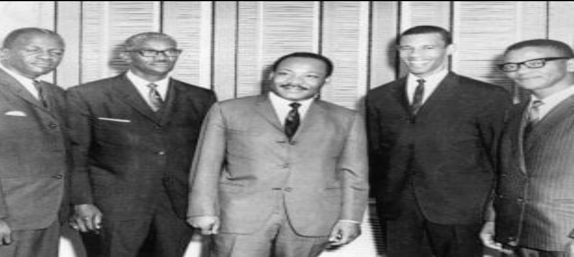 Three men in suits standing indoors, black and white photo.
