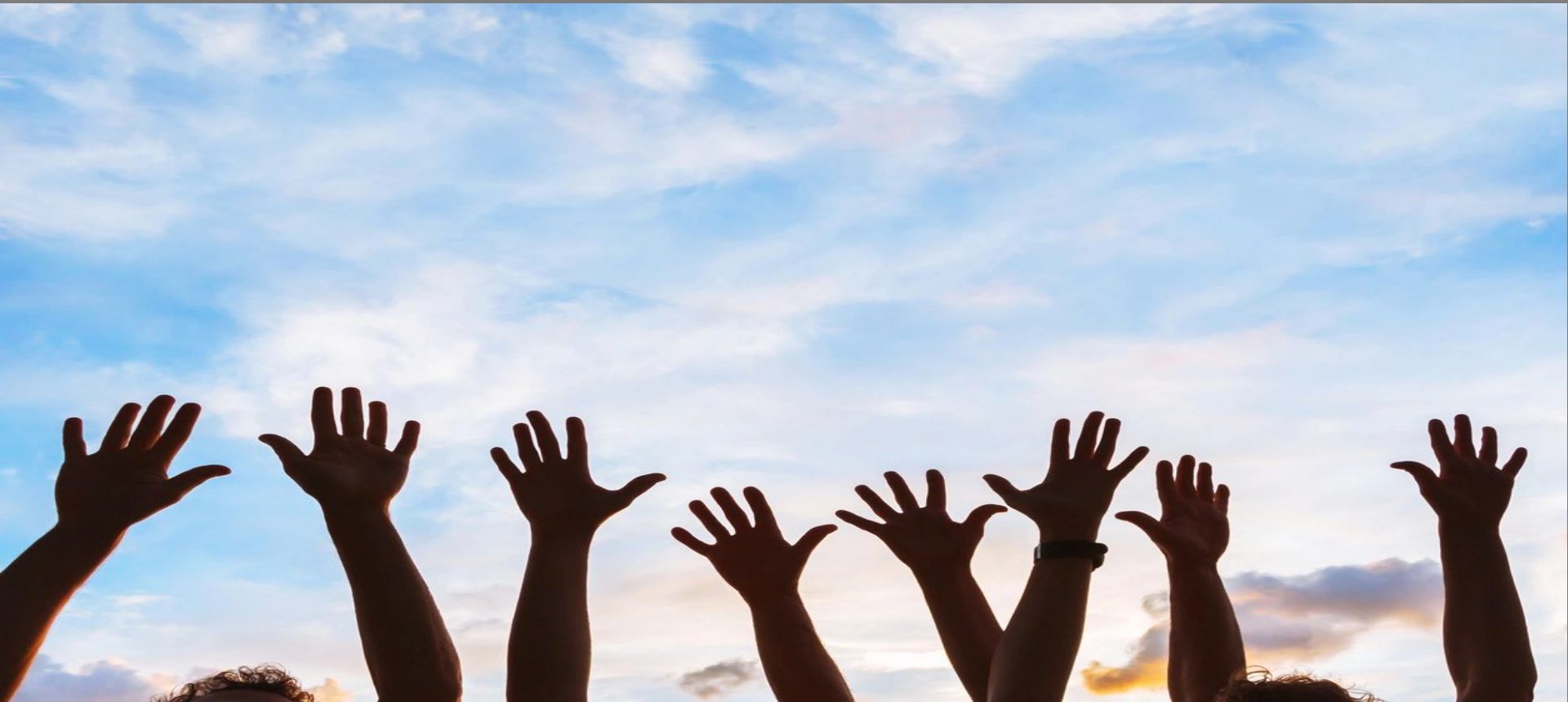 Silhouetted hands reaching up against a blue sky with clouds.